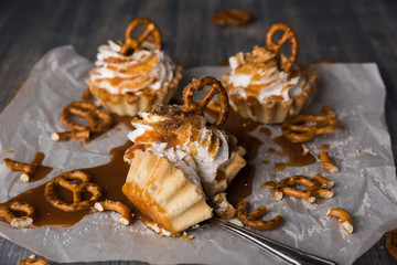 Homemade cupcakes with salted caramel and pretzels.Sweet cakes with syrup and cream cheese on baking paper and wooden table. Spoon