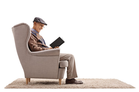 Elderly man seated in an armchair reading a book