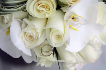 background of beautiful wedding bouquet of roses and orchids and two gold and platinum wedding rings