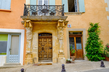 Façade s'une ancienne maison dans le village de Saint-Saturnin les Apt. Les sculpture des Atlantes qui suppotent le balcon. Provence, France. 