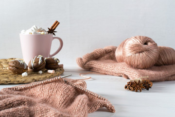 Cup of hot chocolate and marshmallows with cakes. Knitting from rose yarn on a white background