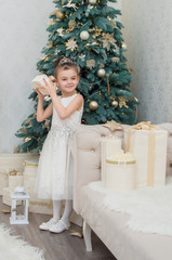 cute little girl in white dress holding a gift on Christmas Eve in a decorated living room