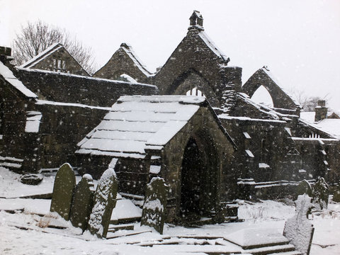picturesque ruined church in falling snow in heptonstall with graveyard and arches