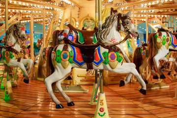 Fototapeta na wymiar Children's merry-go-round in an amusement park with colorful horses decorated with glowing light bulbs