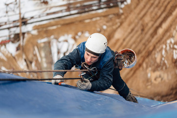 Fototapeta na wymiar Professional industrial climber in helmet and uniform works at height. Risky extreme job. Industrial climbing at construction site