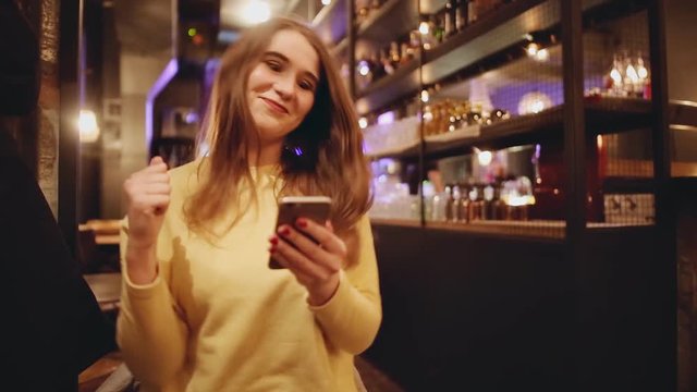 Happy young woman using smart phone and celebrating at restaurant