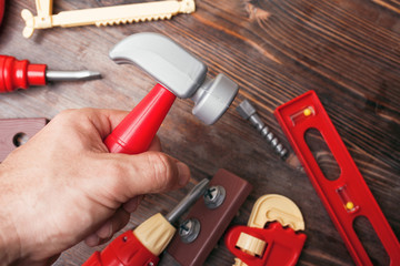 Toy hammer in a man's hand and other tools on a wooden background