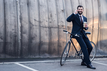 cheerful businessman with coffee to go talking on smartphone on street