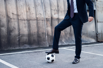 partial view of businessman in suit playing soccer on street