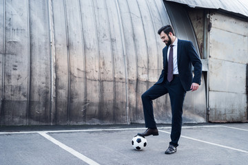 smiling businessman in suit playing soccer on street
