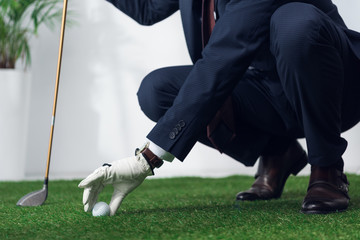 cropped shot of businessman in suit and glove playing golf in office