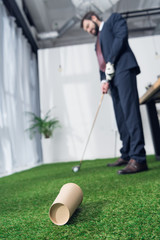 selective focus of young businessman playing golf in office