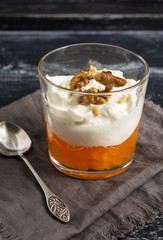 Yoghurt with persimmon and nuts in a glass. Dessert on a wooden table with a spoon and napkin