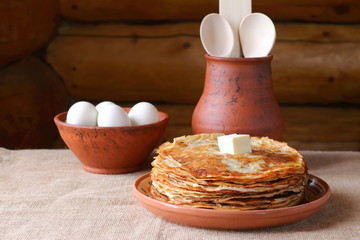 A stack of pancakes. A stack of pancakes in a clay plate on the background of a log wall.
