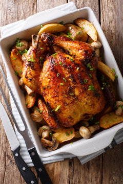 Whole baked chicken with mushrooms and potatoes close-up in a baking dish. vertical top view