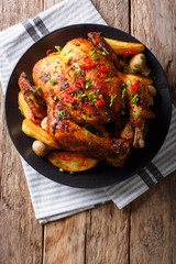 Baked whole chicken with mushrooms and potatoes close-up on a plate. vertical top view © FomaA