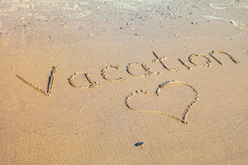 Word Vacation written in the sand on the beach.