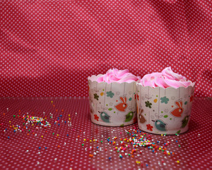 Two cup cake on the red fabric and white dot pattern with colorful rounded sugar beads and reflect floor. cupcake is a small cake baked in a cup-shaped container.