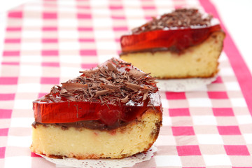 served two slices of fresh baked delicious cherry cheese cake with cherry topping and decorated with chocolate on checkered tablecloth