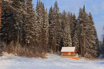 Winter landscape with small wooden house on the edge of the forest .