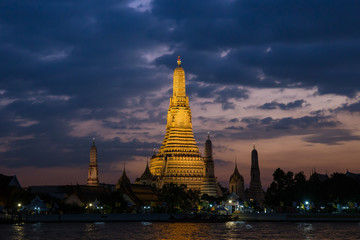 Fototapeta premium Pagoda at temple of dawn or Wat Arun in Bangkok, Thailand when sunset at twilight with scattered cloud and blue sky in the background and Chao Phraya river in the foreground. 