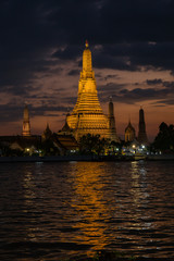 Naklejka premium Pagoda w świątyni świtu lub Wat Arun w Bangkoku w Tajlandii, kiedy zachód słońca o zmierzchu z rozproszoną chmurą i błękitne niebo w tle i rzeka Chao Phraya na pierwszym planie.