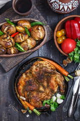 Whole roast chicken in an iron pan on dark background, top view.