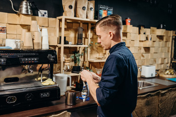 Handsome barista preparing cup of coffee for customer in coffee shop. Retro picture with little noise.