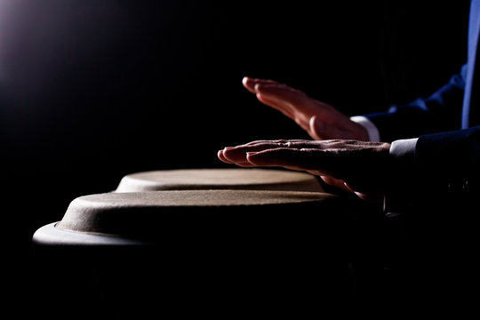 Hands of a musician playing on bongs in dark tones