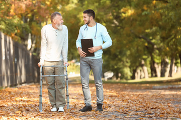 Young caregiver walking with senior man in park