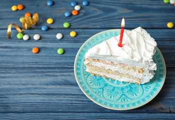 Piece of birthday cake with candle on table