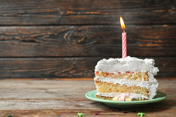 Piece of birthday cake with candle on table