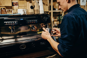 Handsome barista preparing cup of coffee for customer in coffee shop. Retro picture with little noise.