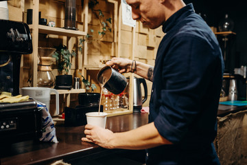 Handsome barista preparing cup of coffee for customer in coffee shop. Retro picture with little...