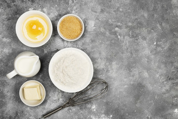 Ingredients for pastries - flour, eggs, butter, milk, sugar on a gray background. Top view, copy space. Food background