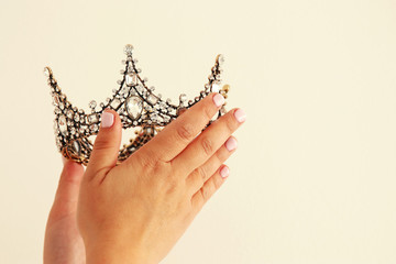 Woman's hand holding a crown for show victory or winning first place. White background. Copy space. Isolated.