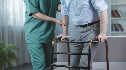 Melancholy man standing up and moving with walking frame at nursing home