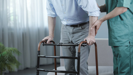 Senior patient of nursing home moving with walking frame and nurse support