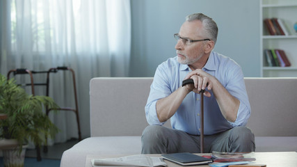 Retired male sitting on sofa at nursing home and thinking about life, sadness