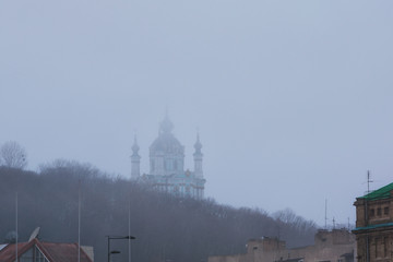 Obraz premium Mysterious view to St. Andrew's Church (one of the main attractions of the city) in rich fog, mist background. Morning city scape. Kyiv, Ukraine