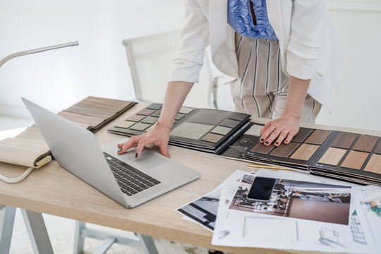 Hands of unrecognisable woman interior designer working with material palette and typing on her laptop.