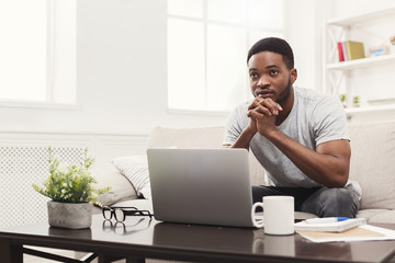 Young thoughtful man at home messaging online on laptop