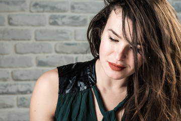 Beauty fashion portrait of beautiful young hair model. Close up portrait of young woman with fresh daily make up looks down. White brick wall background.