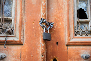 Rusty padlock on an old wooden door with broken window. Close up view with details.