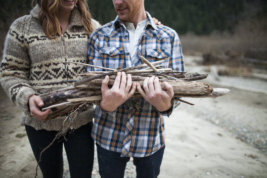 Midsection of boyfriend holding firewood while standing beside girlfriend at campsite