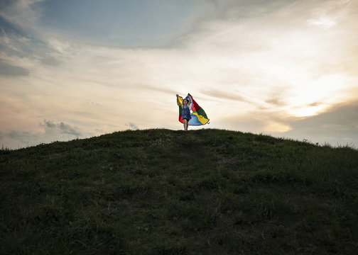 Low angle view of playful girl holding multi colored textile while running on hill against cloudy sky