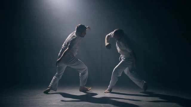 Two men practicing capoeira in dark room. Slow motion