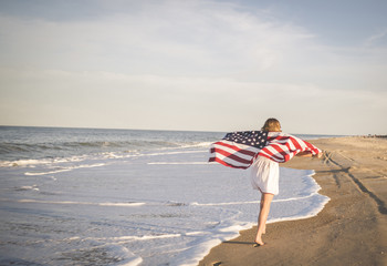 Rear view of girl holding American flag while running on beach
