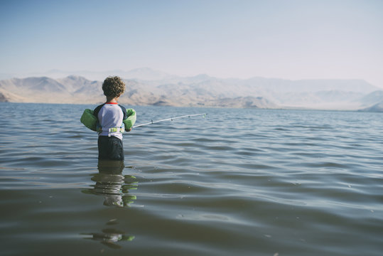 Rear view of boy fishing while standing in river against clear sky during sunny day