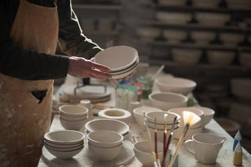 Mid section of male potter holding bowls